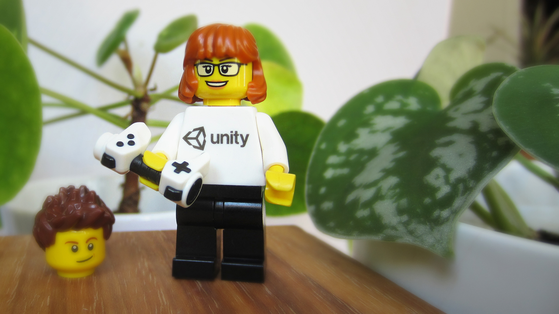 A lego minifigure wearing a with a white with a Unity logo on it's chest holding a video game controller