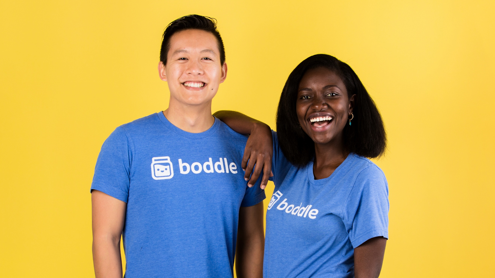 Two people wearing blue Boddle shirts standing in front of a yellow background