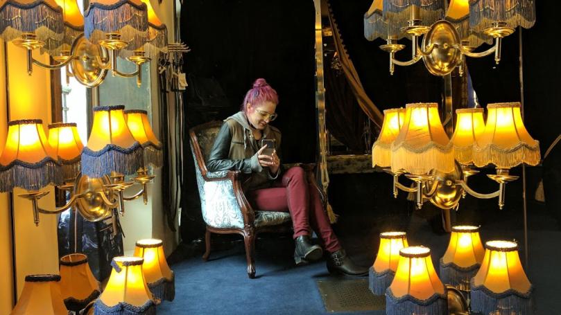 Kylie sitting in a chair taking a photo in a mirror surrounded with lights.