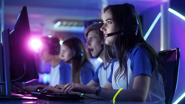 Professional gamer (female) and her team participate in an eSports cyber games tournament. She has her headphones on and, as a team leader, commands strategical maneuvers into a microphone.
