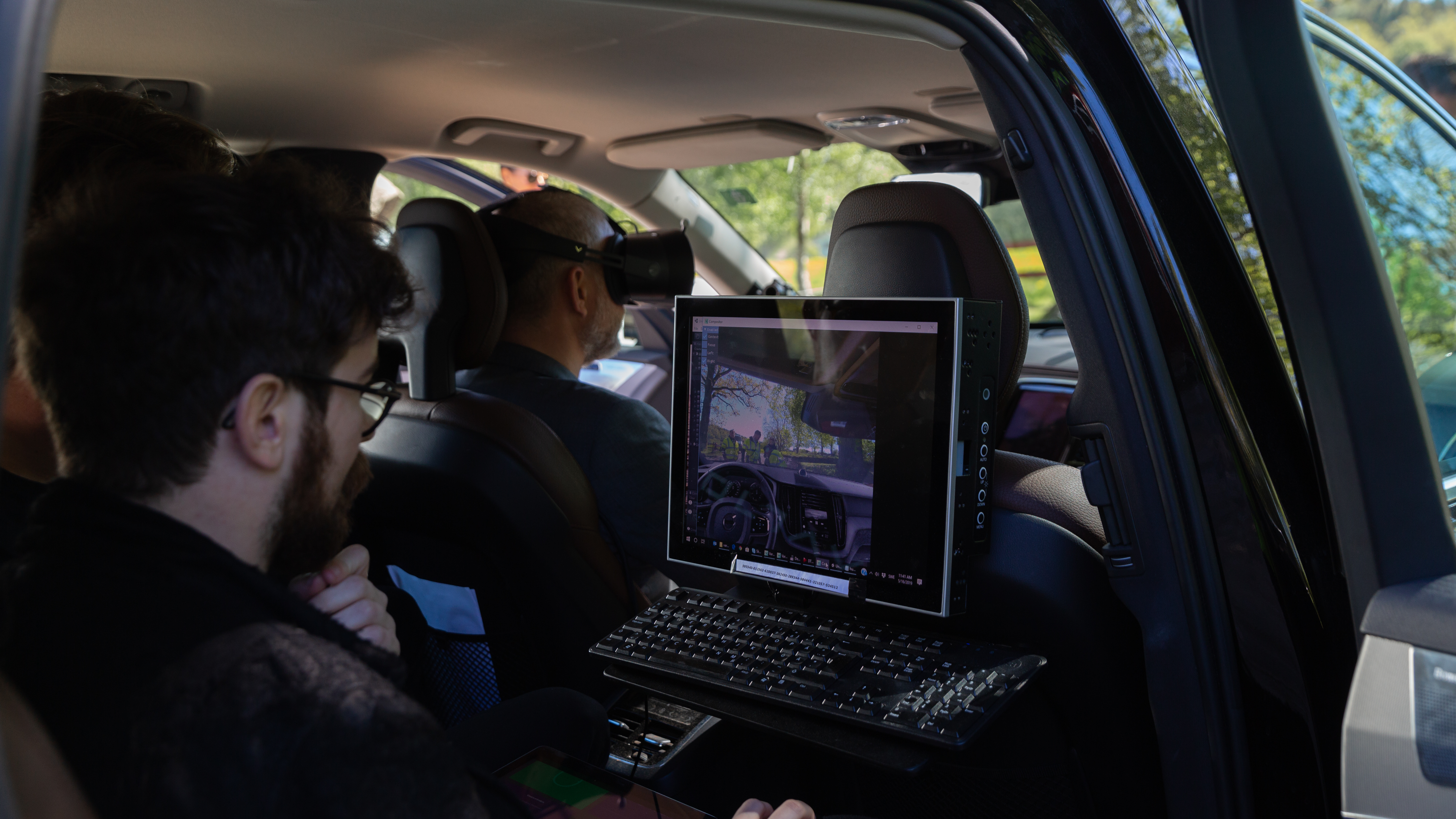 Rear seat passenger uses a laptop to control a mixed reality experience for the vehicle driver, who wears a headset.