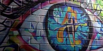 Street art depicting a large, multi-colored eye on a brick wall.
