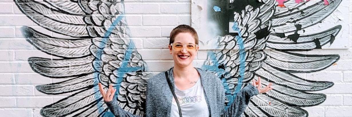 Kylie posing in front of a wall with painted wings.