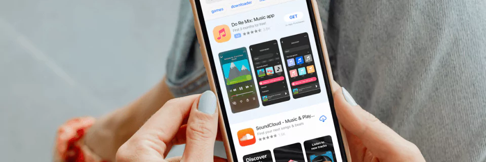 Image of a person’s hands holding an iPhone above crossed legs, searching “music” in the App Store
